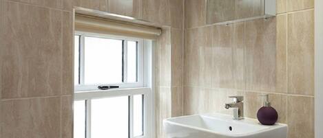 A bathroom with beige tiles, a window with a white blind, a white sink, and a purple soap dispenser.