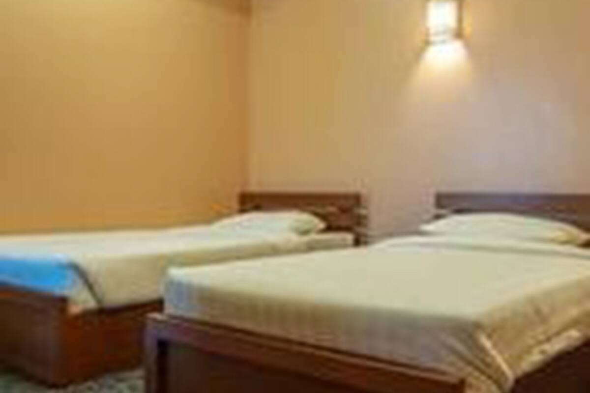 Quarto de hotel com duas camas de solteiro, piso coberto por carpete e luminária fixa na parede.