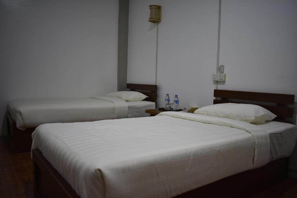 Two single beds with white bedding, a bedside table with a bottle and a glass, and a wall-mounted light fixture.