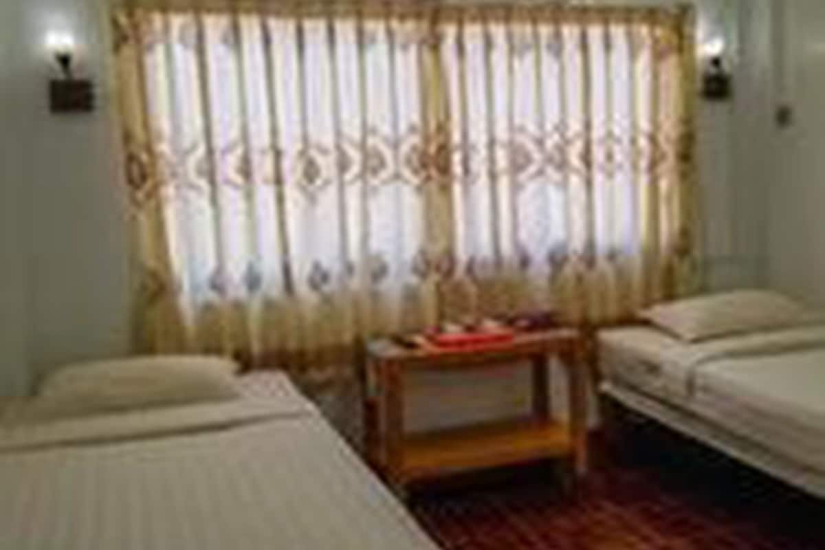 Quarto com duas camas, uma mesinha e uma cortina.