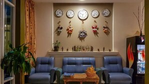 Un salón con sofás azules, una mesa de centro y una pared decorada con relojes y adornos colgantes.