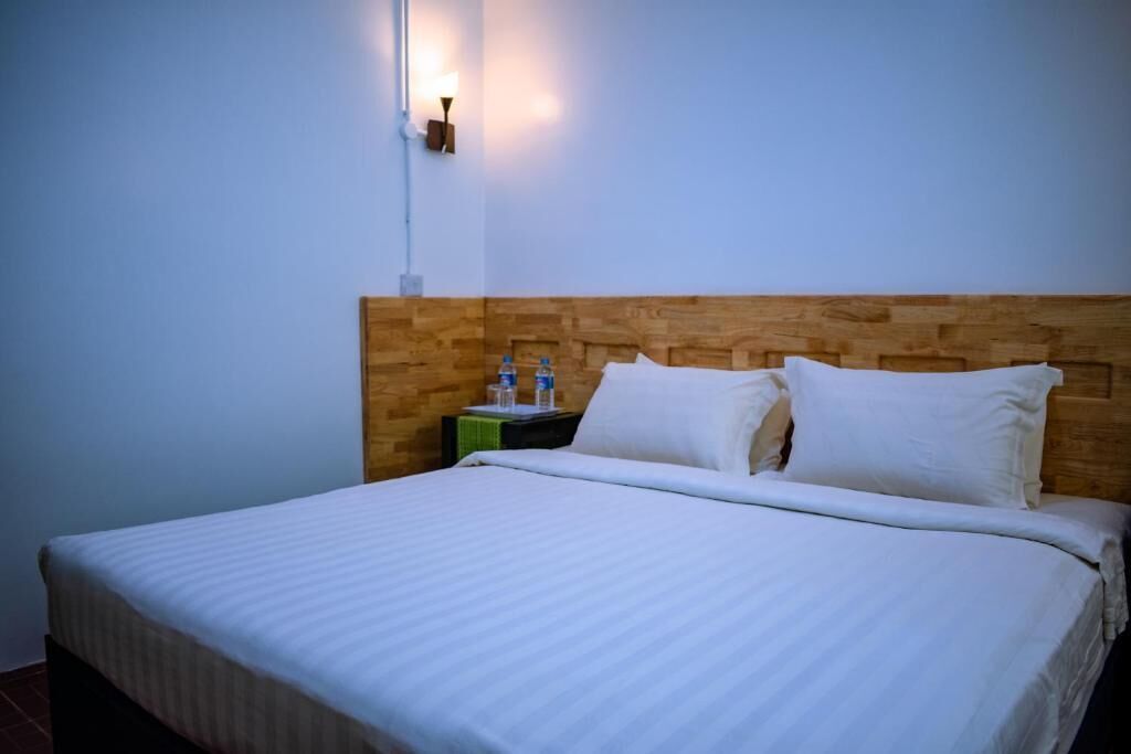 Una cama bien tendida con sábanas blancas en una habitación con cabecera de madera y una lámpara de pared.