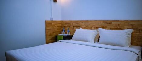 Una cama bien tendida con sábanas blancas en una habitación con cabecera de madera y una lámpara de pared.