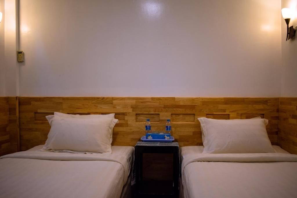 Habitación de hotel con dos camas, cabecero de madera, lámparas de noche y una mesita con botellas de agua.