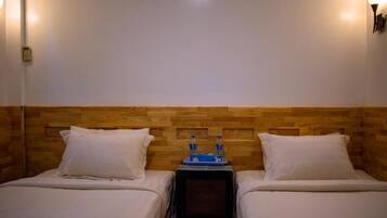 Habitación de hotel con dos camas, cabecero de madera, lámparas de noche y una mesita con botellas de agua.