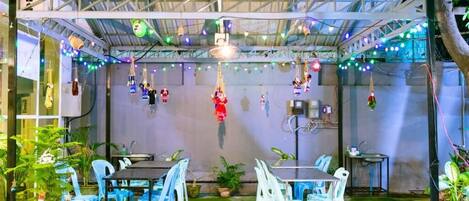 An outdoor patio with tables and chairs, string lights, and hanging decorations.