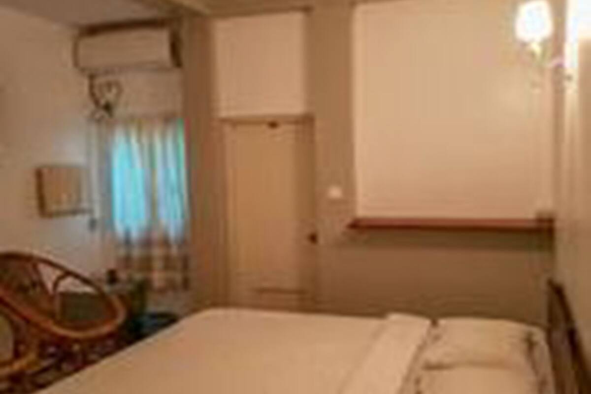 Quarto de hotel com uma cama, mesa de cabeceira, cadeira e janela com cortinas.
