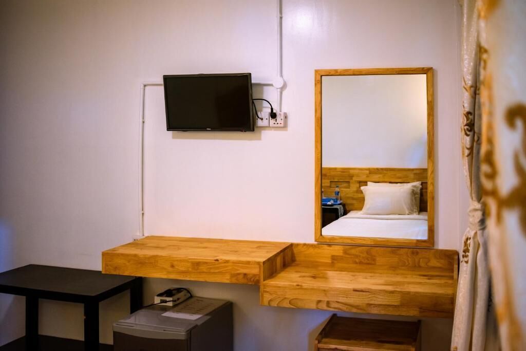 Ein gemütliches Hotelzimmer mit Schreibtisch aus Holz, einem wandmontierten Flachbildfernseher und einem großen Spiegel, der ein Bett mit weißer Bettwäsche reflektiert.
