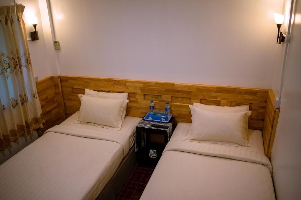 Una habitación pequeña y acogedora con dos camas individuales, cabecero de madera, lámparas de noche y una mesita con bandeja.