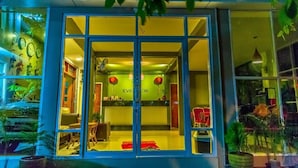 Entrada de un hotel con mostrador de recepción, una silla roja y plantas en macetas.