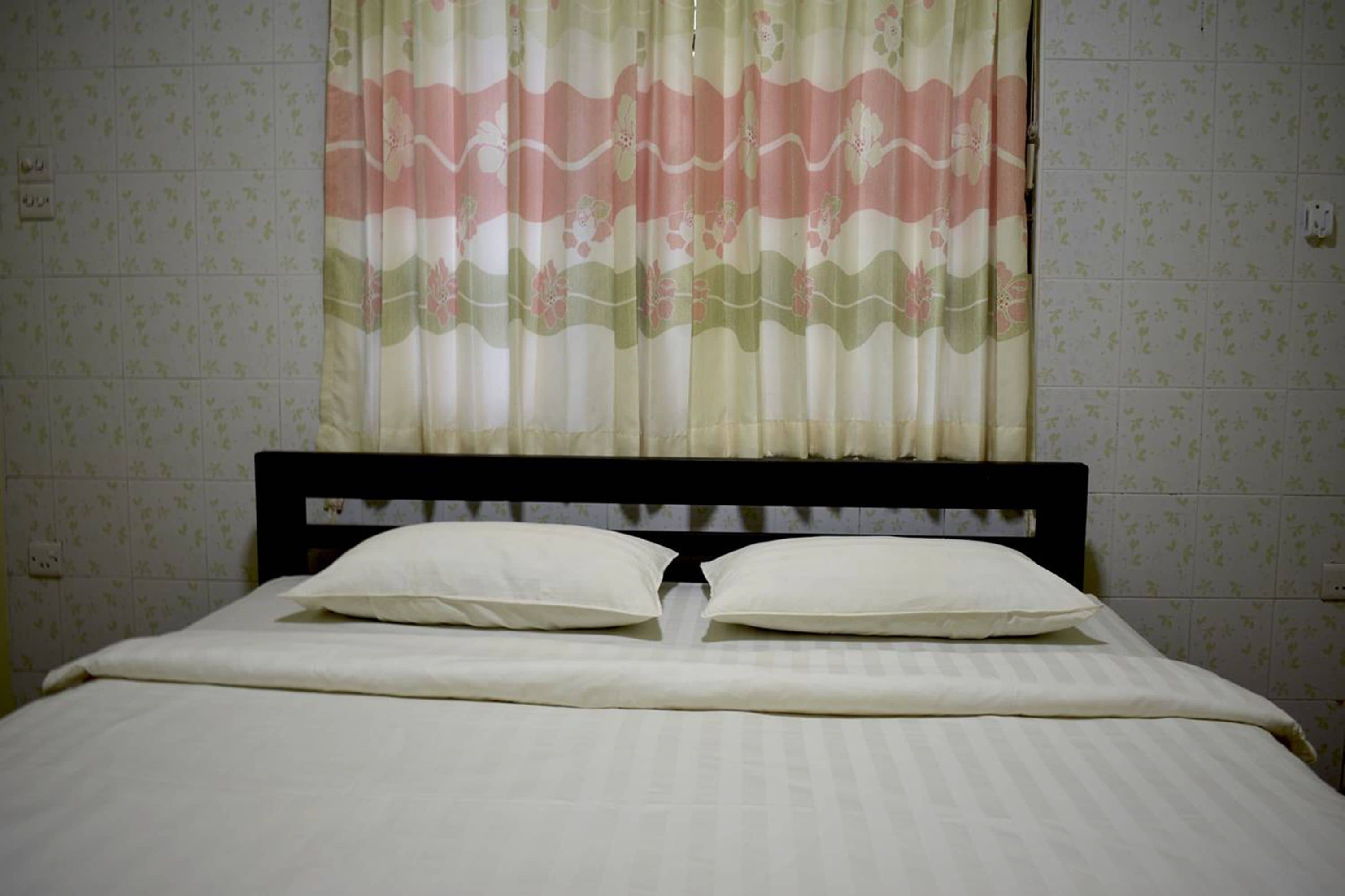 Una cama con ropa blanca y dos almohadas, un cabecero de madera y una cortina con estampado floral.