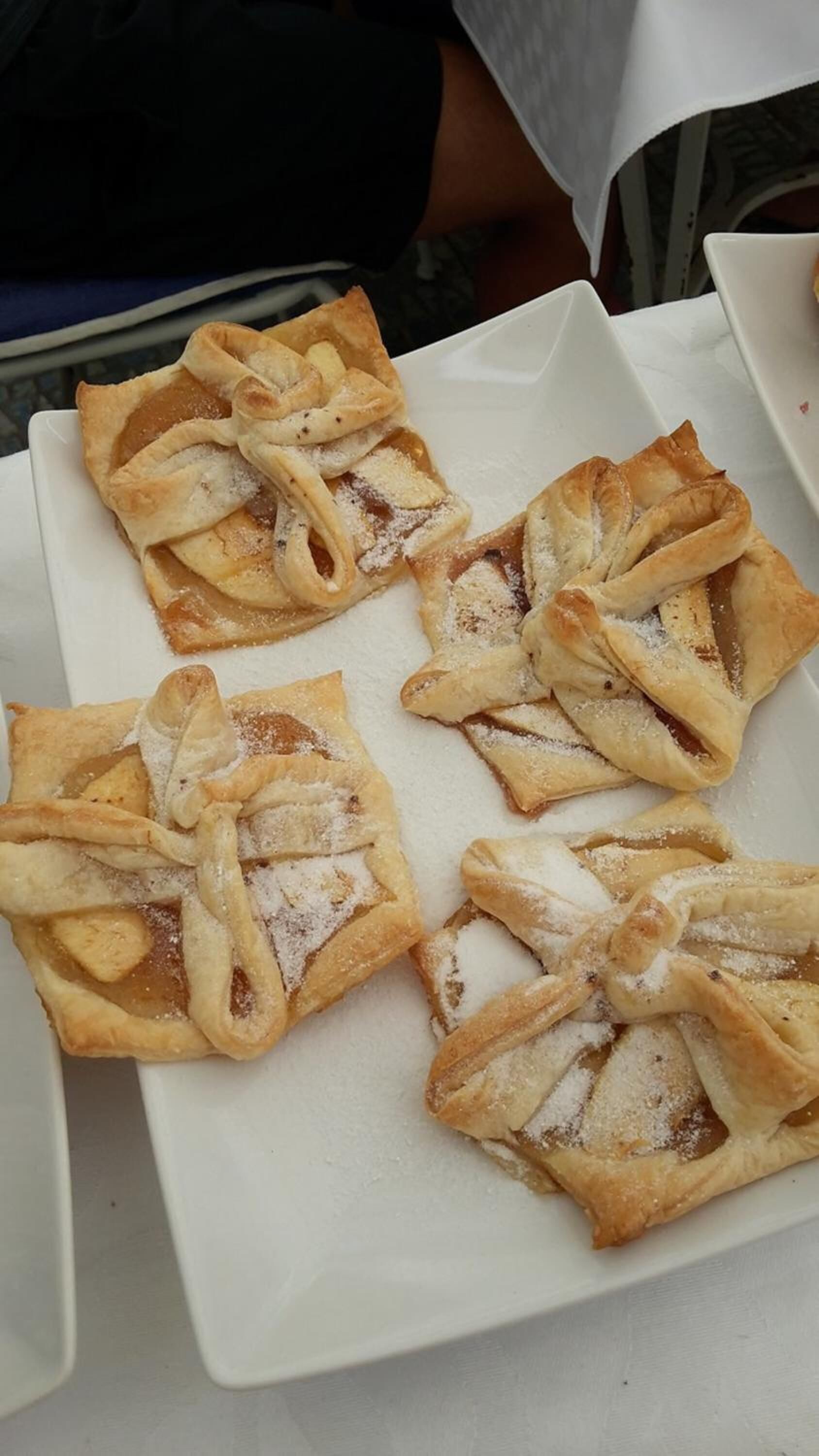 A white plate with four pastries dusted with powdered sugar.