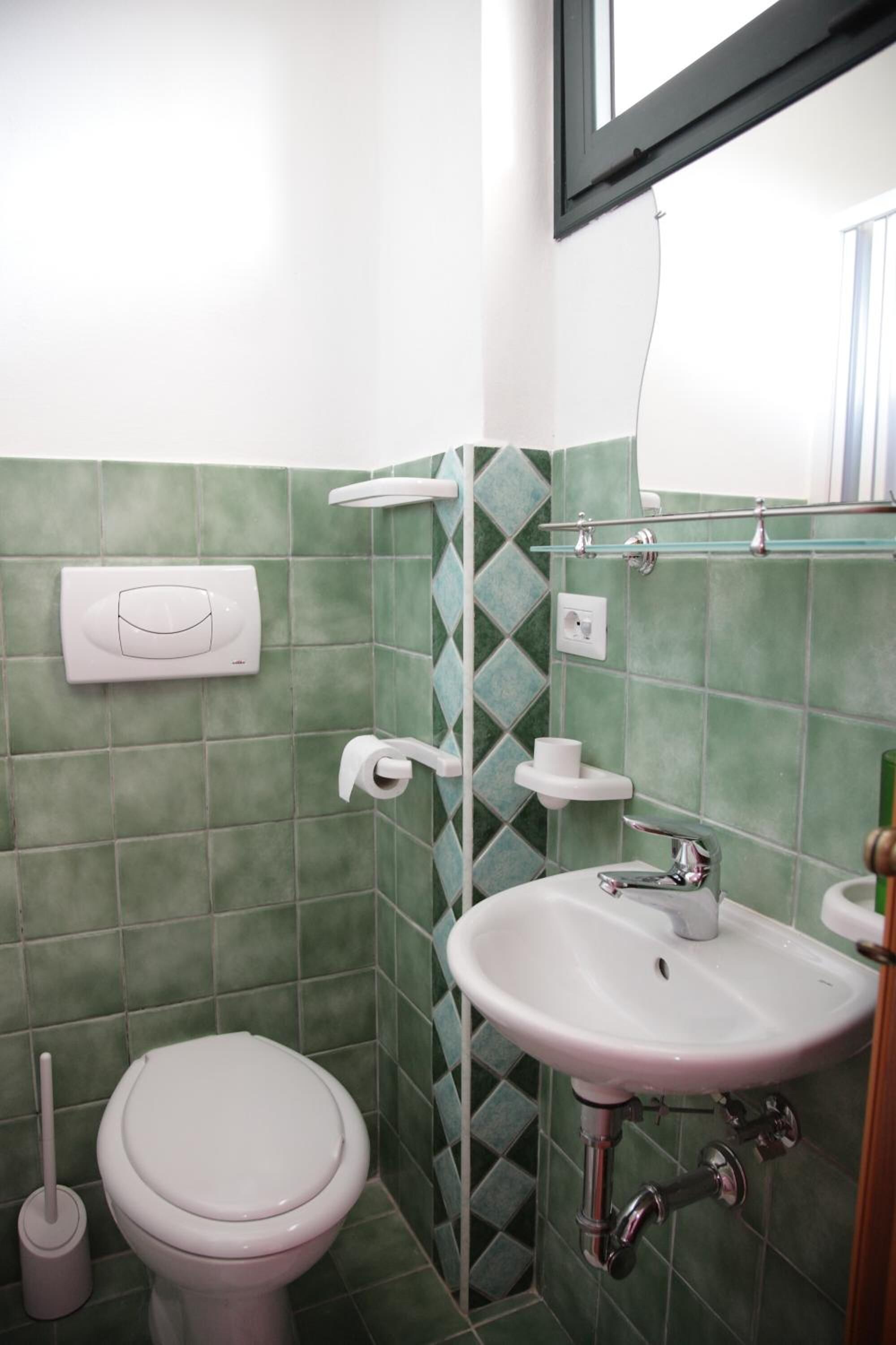 Un baño con inodoro, lavamanos y paredes de azulejos verdes.
