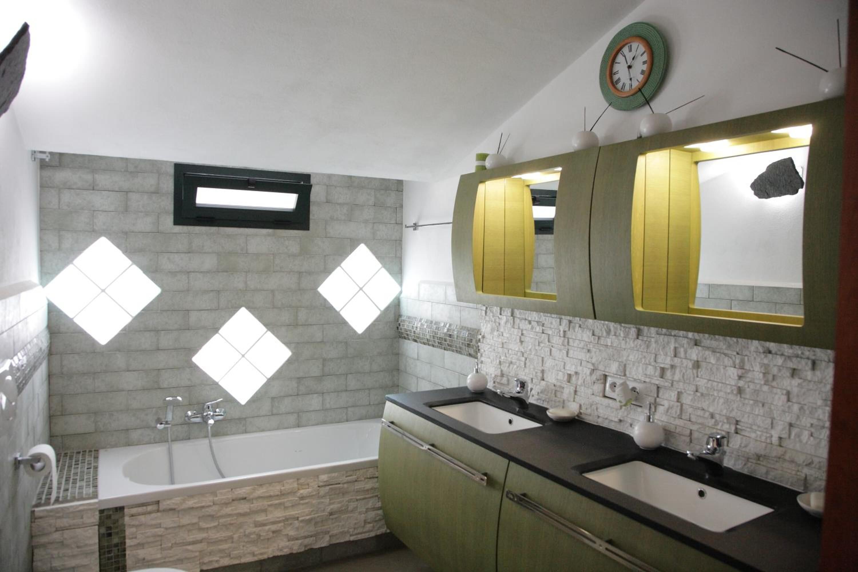 A bathroom with a bathtub, two sinks, a mirror, and a clock on the wall.