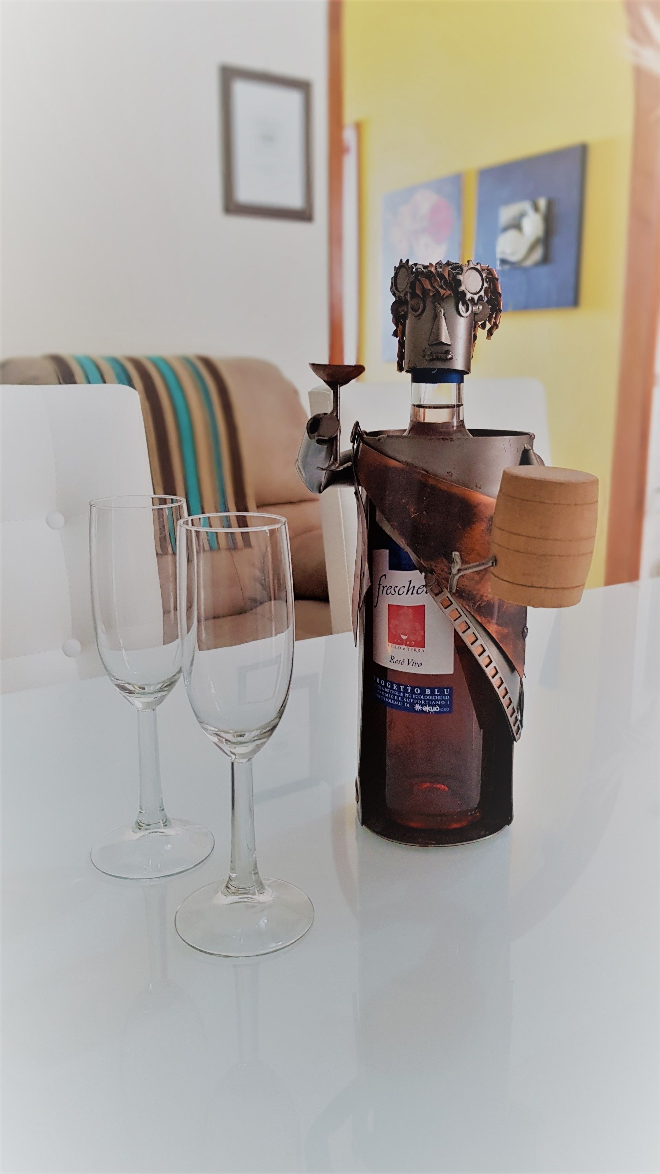 A bottle of Fresche on a white table with two empty wine glasses.