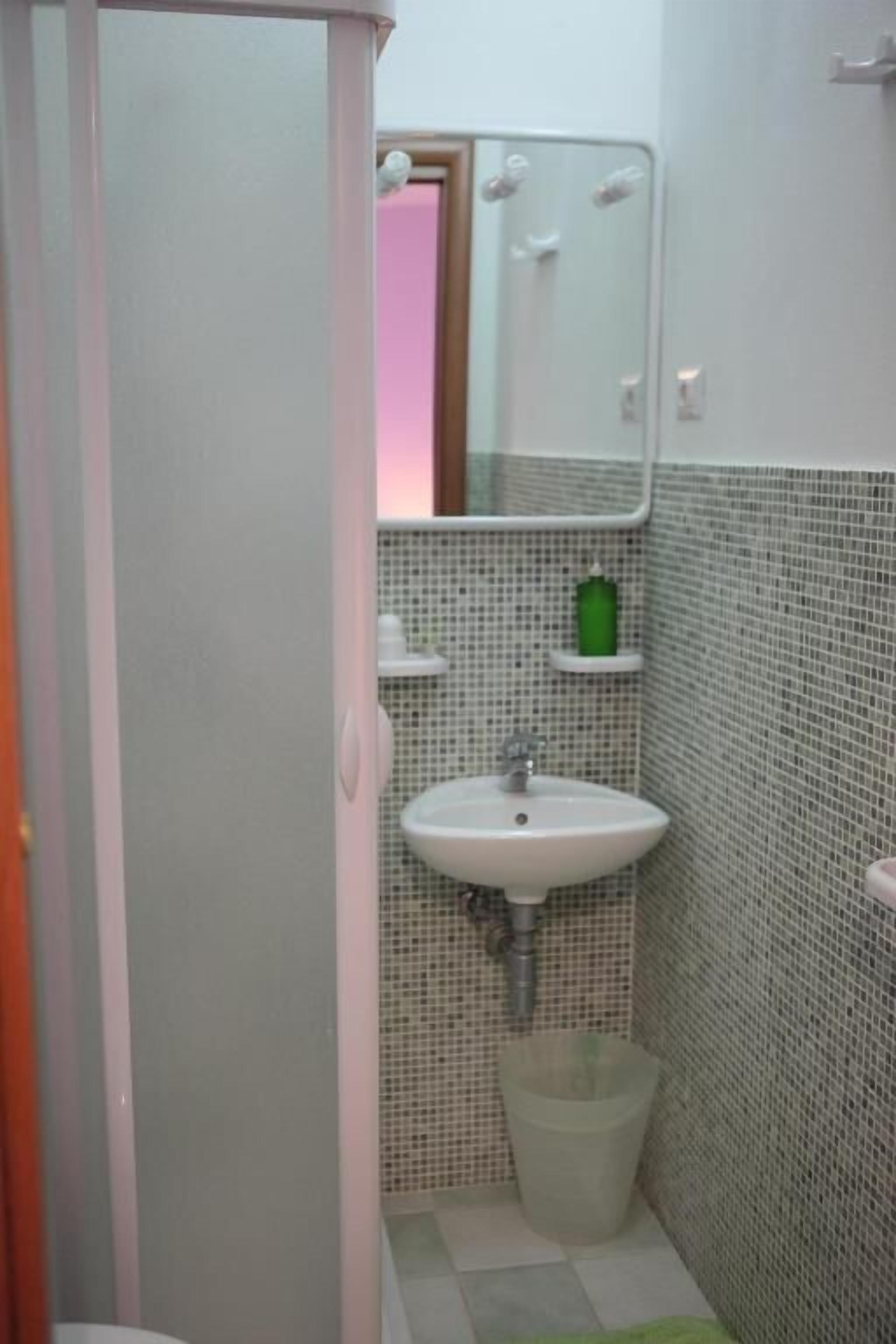 Un baño con un lavamanos blanco, un espejo y una pared con azulejos.