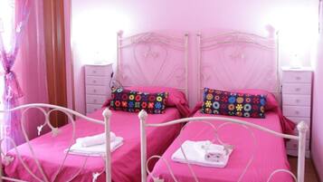 Un dormitorio decorado en tonos rosas, con dos camas, un ventilador de techo y un equipo de aire acondicionado.