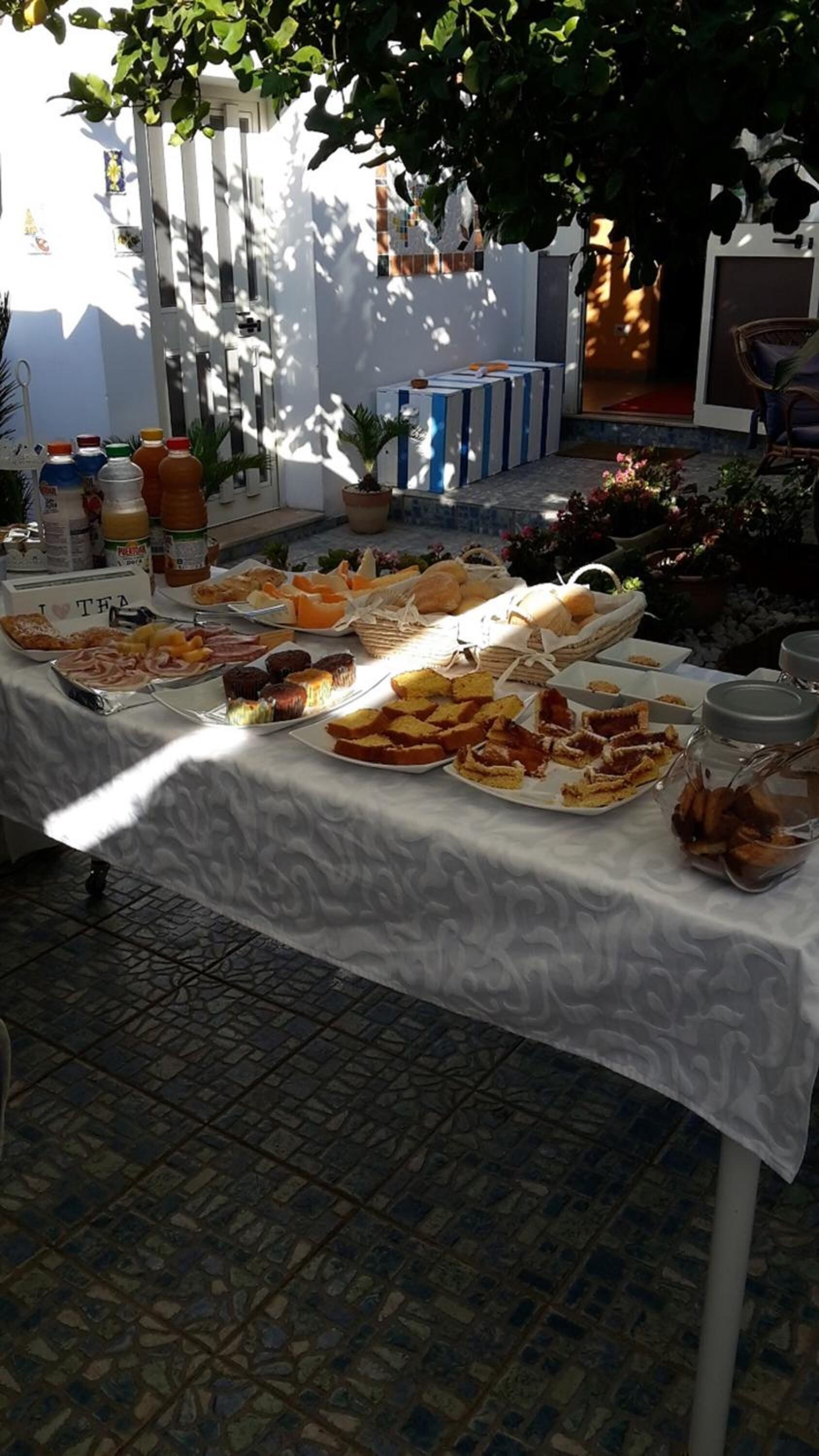 A table with various food items and beverages, set outdoors with a white tablecloth.