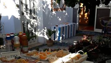 A table with various food items and beverages, set outdoors with a white tablecloth.