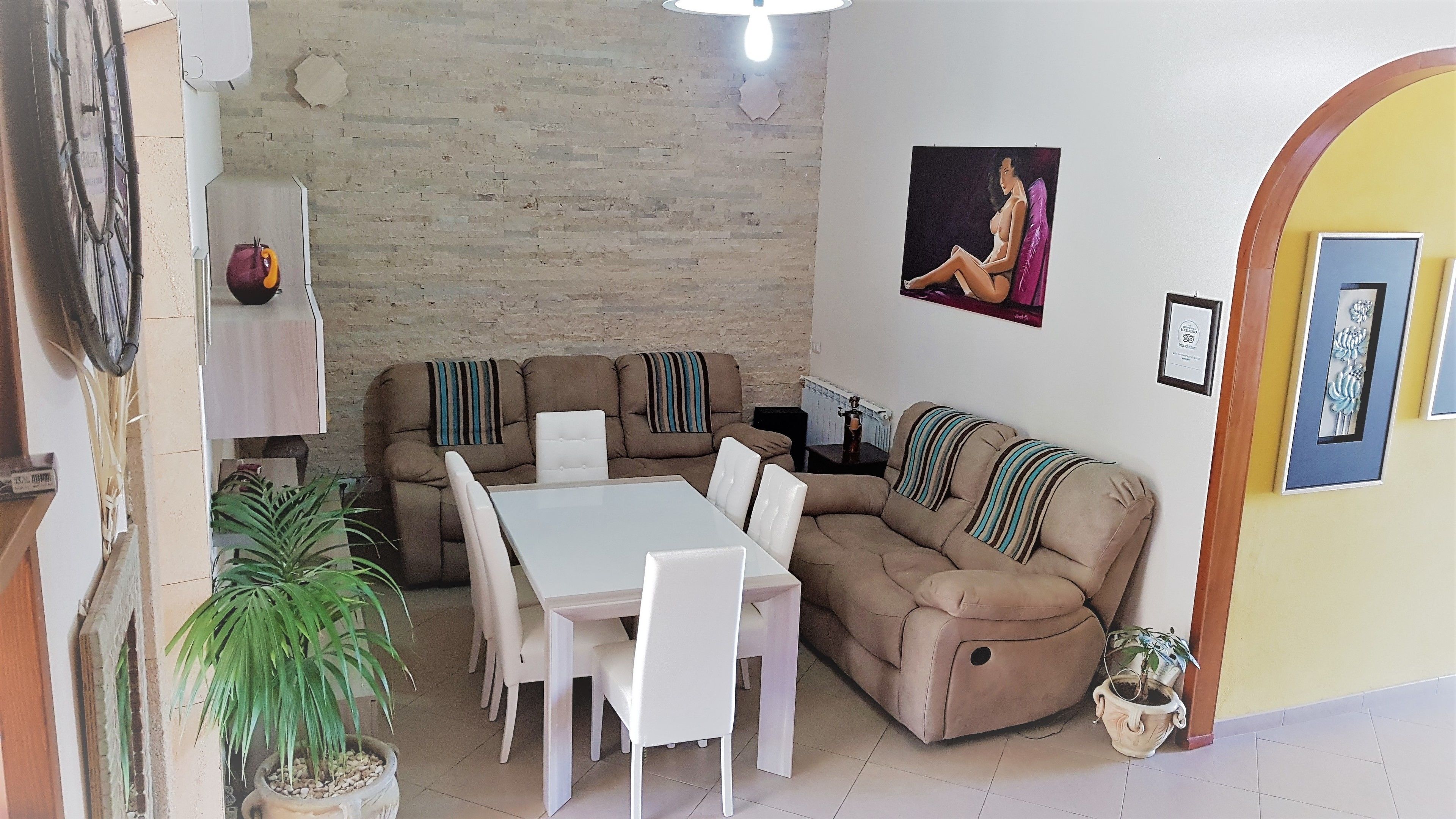 A living room with a sofa, a dining table, and chairs. There is a potted plant and a wall with a picture.