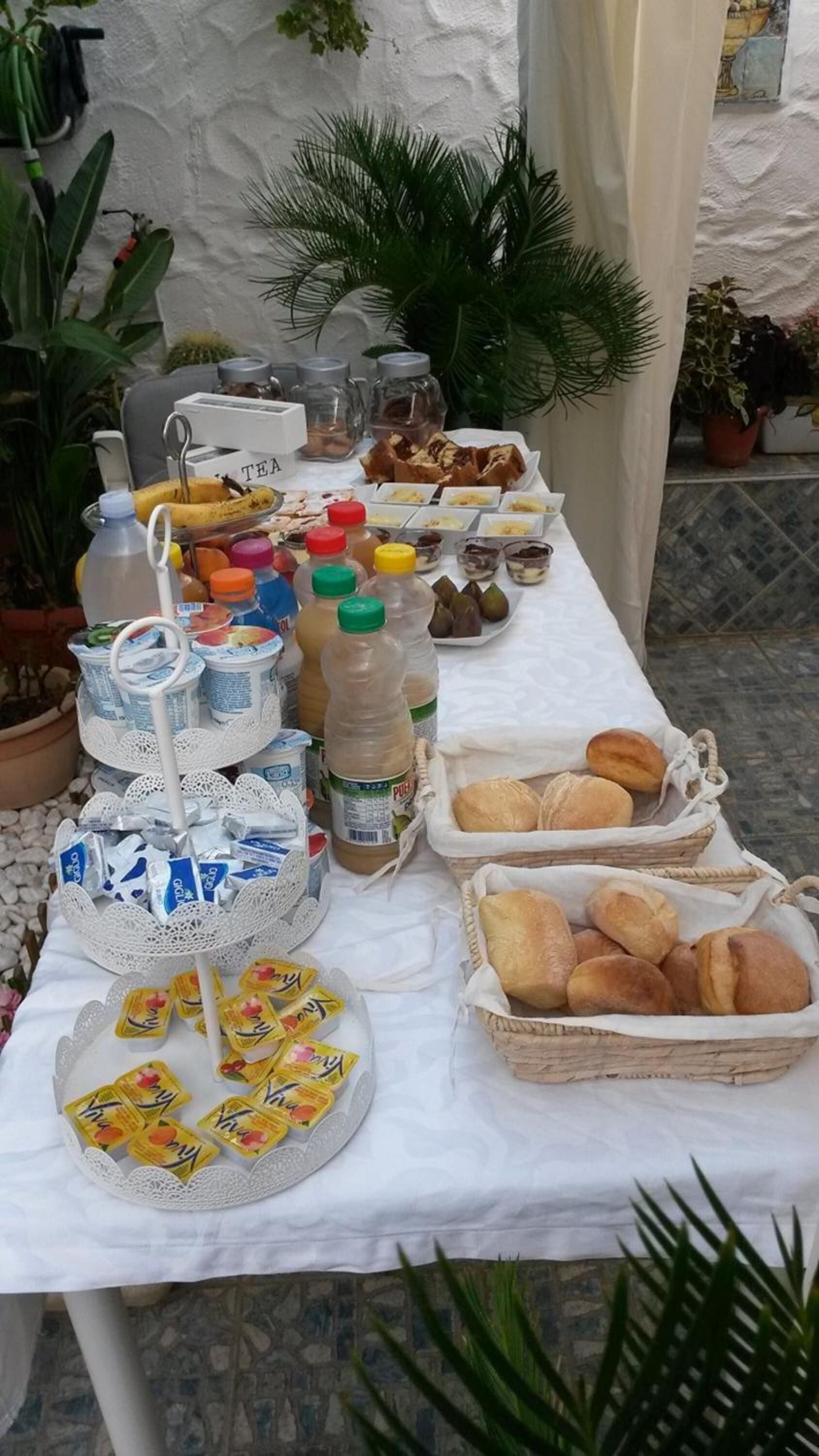 A table with various food items and beverages, including jars of jam, bottles of juice, and baskets of bread.