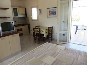 A compact kitchen with a dining area, a television, and a sliding glass door leading to an outdoor patio.