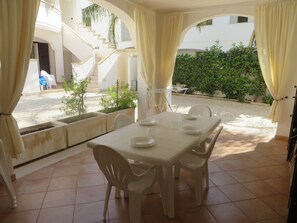 A dining area with a table set for four, white plastic chairs, and a view of a staircase and greenery outside.