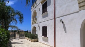 A building with white walls, multiple windows with shutters, and a gated entrance. - Residence Giglio Torre Pali (Salve)