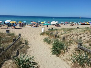 A sandy beach with a wooden fence, beach umbrellas, and people relaxing.