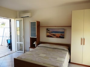 A bedroom with a bed, a wardrobe, a painting, and a sliding door leading to an outdoor area.