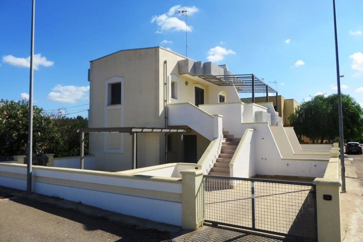 A modern two-story building with a flat roof, a staircase leading to the upper level, and a gated entrance.