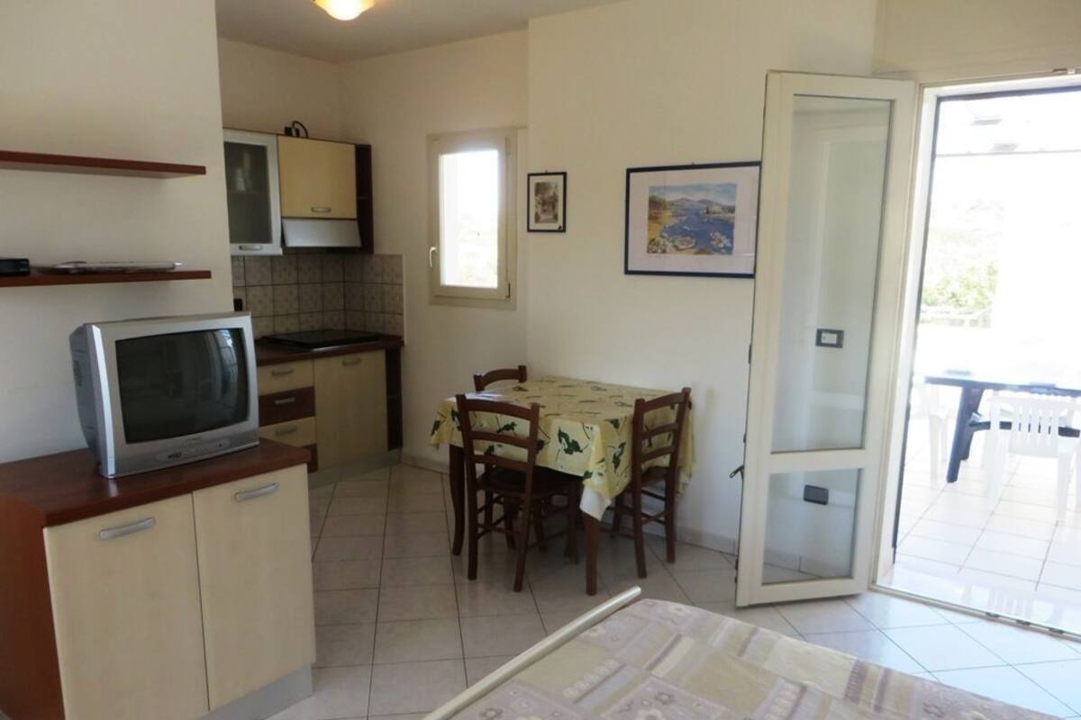 A compact kitchen with a dining area, a television on a cabinet, and a door leading to an outdoor patio.