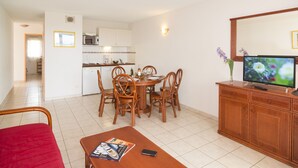 A room with a dining table, chairs, a TV, a cabinet, and a red chair. - Vacancéole - Palmyra Golf (Agde)