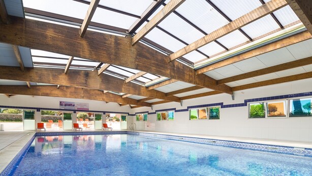 An indoor swimming pool with a skylight ceiling, clear glass windows, and a tiled pool edge. - Vacancéole - Palmyra Golf (Agde)