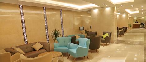 A modern lobby with a reception desk, seating area, and a large potted plant.