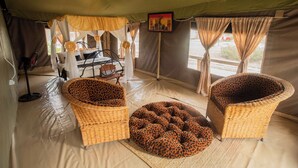 A tented room with two leopard-print armchairs, a bed with a canopy, and a painting on the wall.