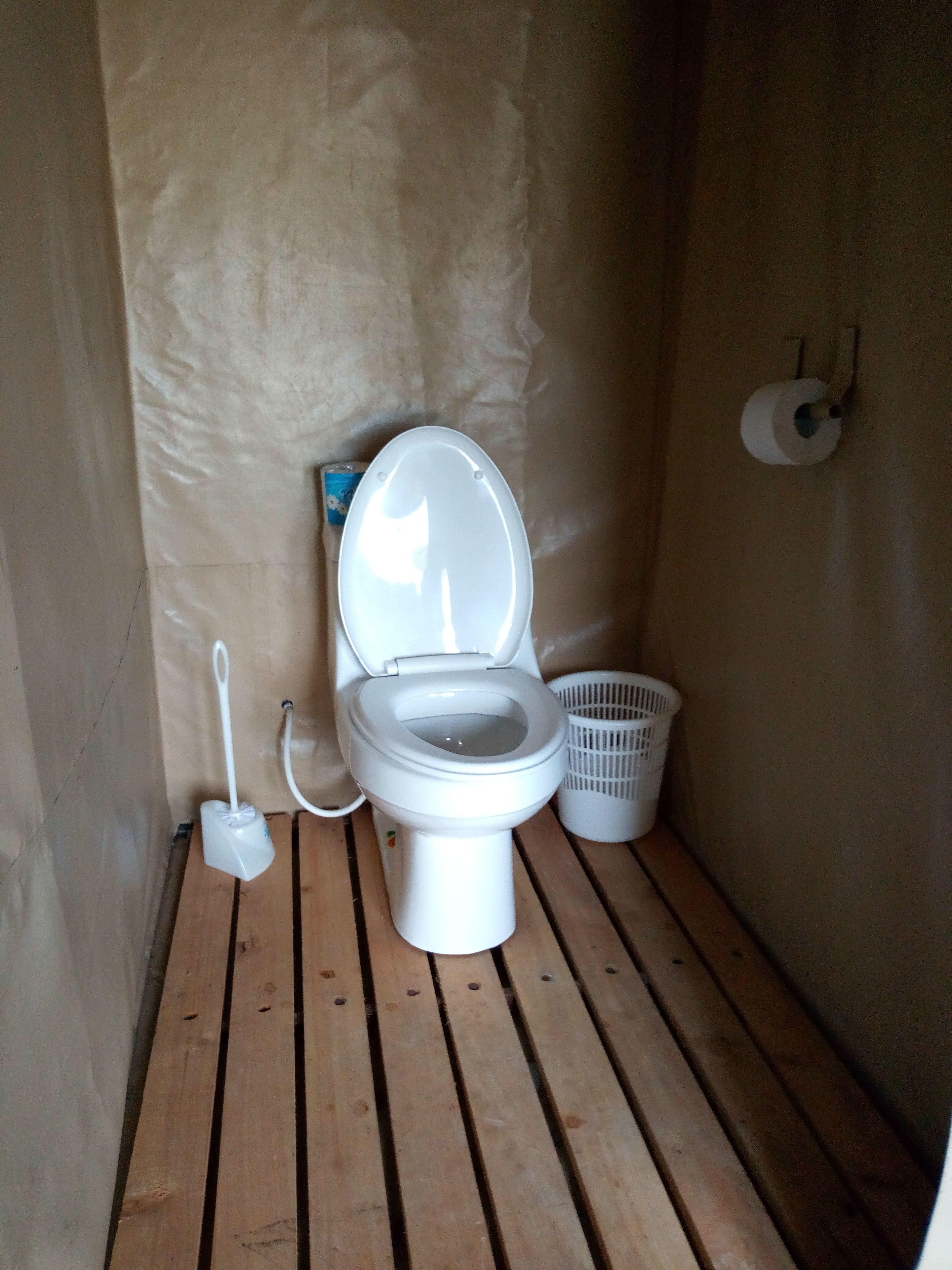 Une petite salle de bain aux dimensions réduites, avec des toilettes blanches, une brosse de toilette blanche et un panier en plastique blanc.