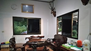 A dining area with a wooden table and chairs, a clock, and a deer head mounted on the wall. - Happy Home Resort (Khlong Yai)