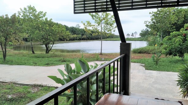 A wooden deck with a railing overlooking a lake, surrounded by greenery and trees. - Happy Home Resort (Khlong Yai)