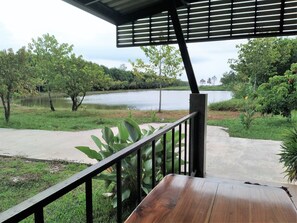 A wooden deck with a railing overlooking a lake, surrounded by greenery and trees. - Happy Home Resort (Khlong Yai)