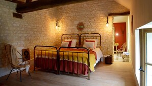A rustic bedroom with a stone wall, a wooden ceiling, a metal bed frame, and a wicker chair. - Domaine de l'Ocrerie (Pourrain)
