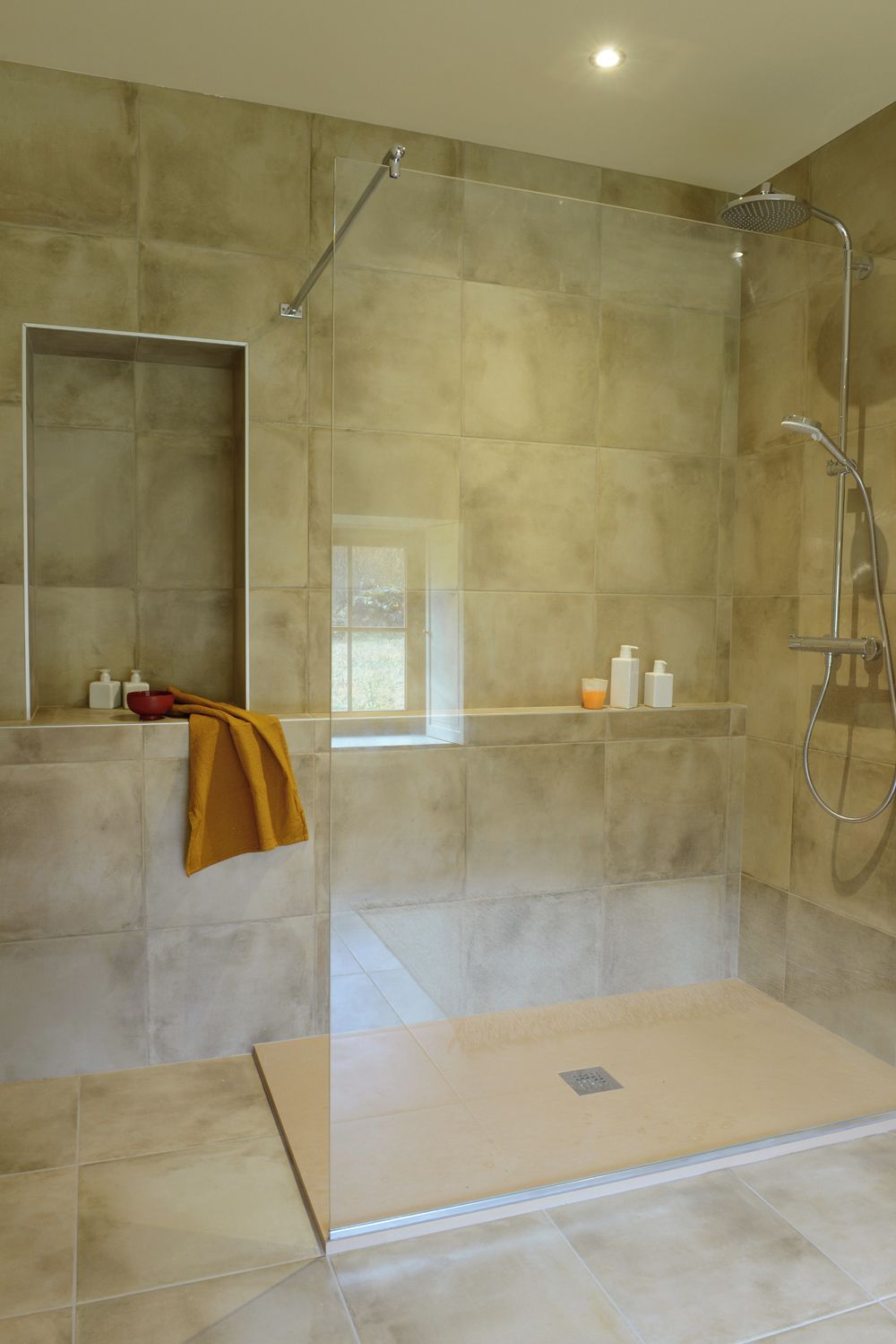 Un espace douche moderne doté d’une porte en verre, d’une barre d’appui et d’un pommeau de douche.