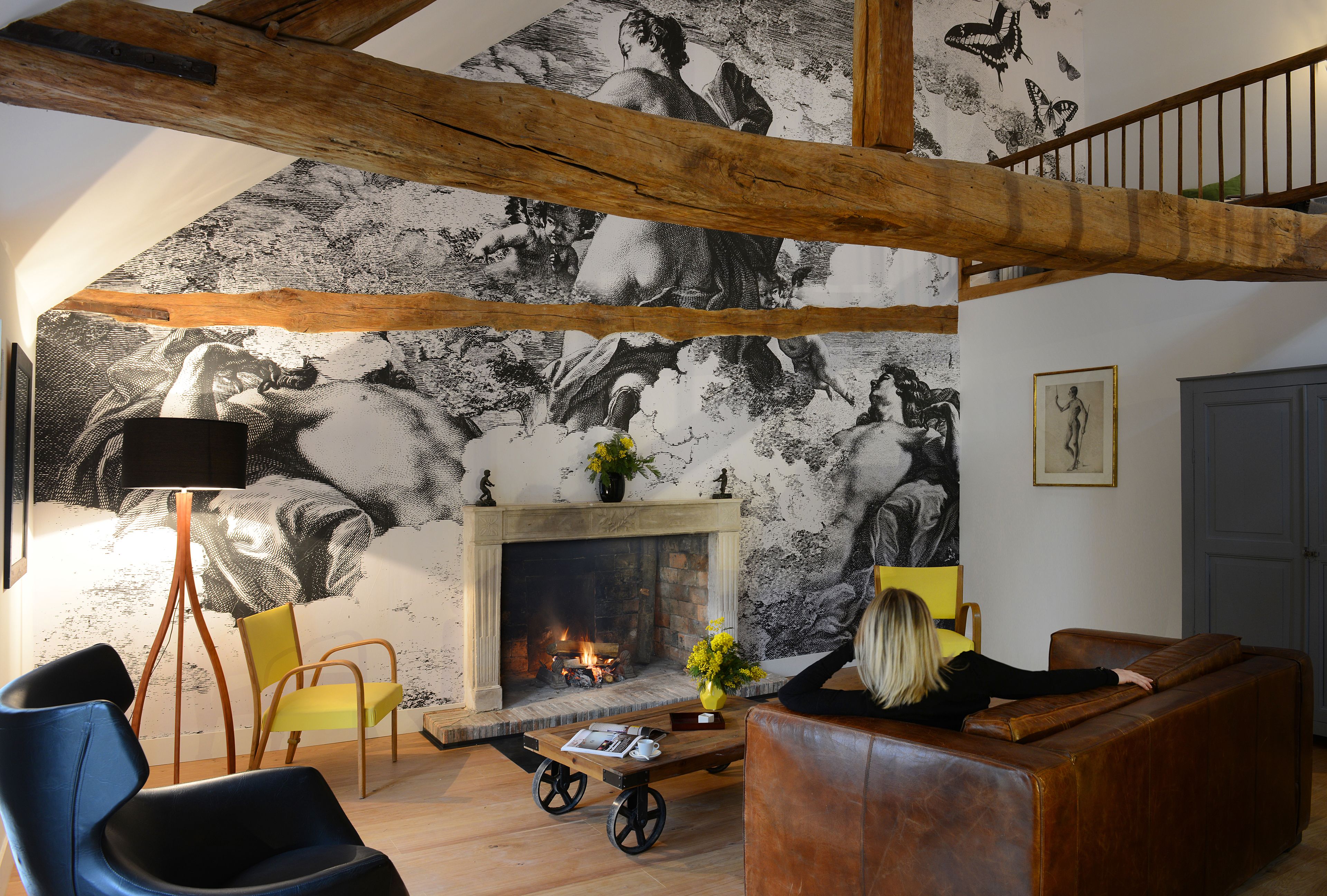 Ein Wohnzimmer mit Kamin, Holzbalken, einer Couch, einem Sessel und einer Stehlampe.