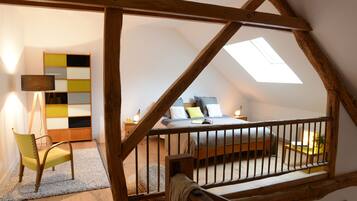 A bedroom with a sloped ceiling, a skylight, a bed, a bedside table, a chair, and a colorful cabinet.