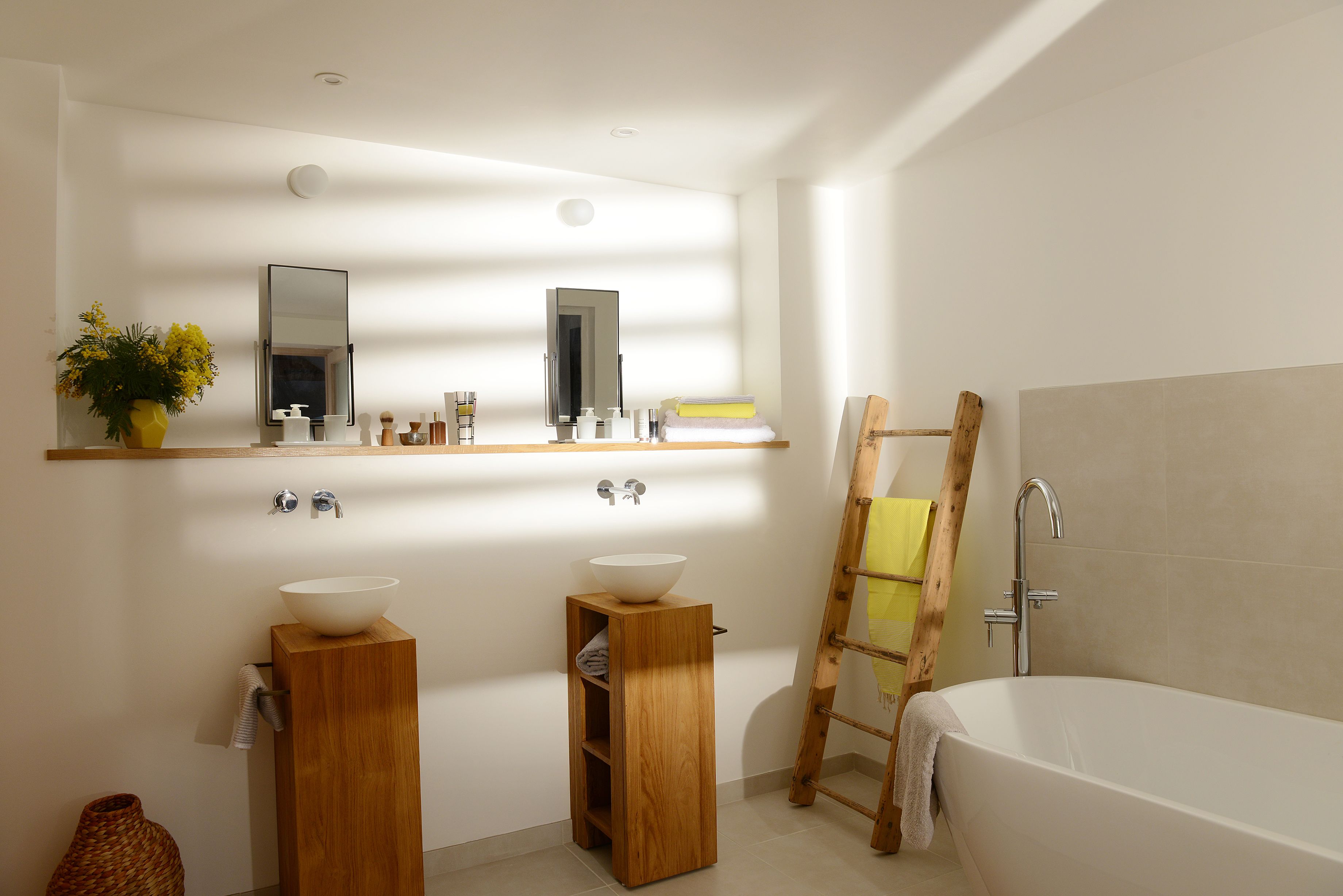 A modern bathroom with two sinks, a large mirror, and a wooden ladder.