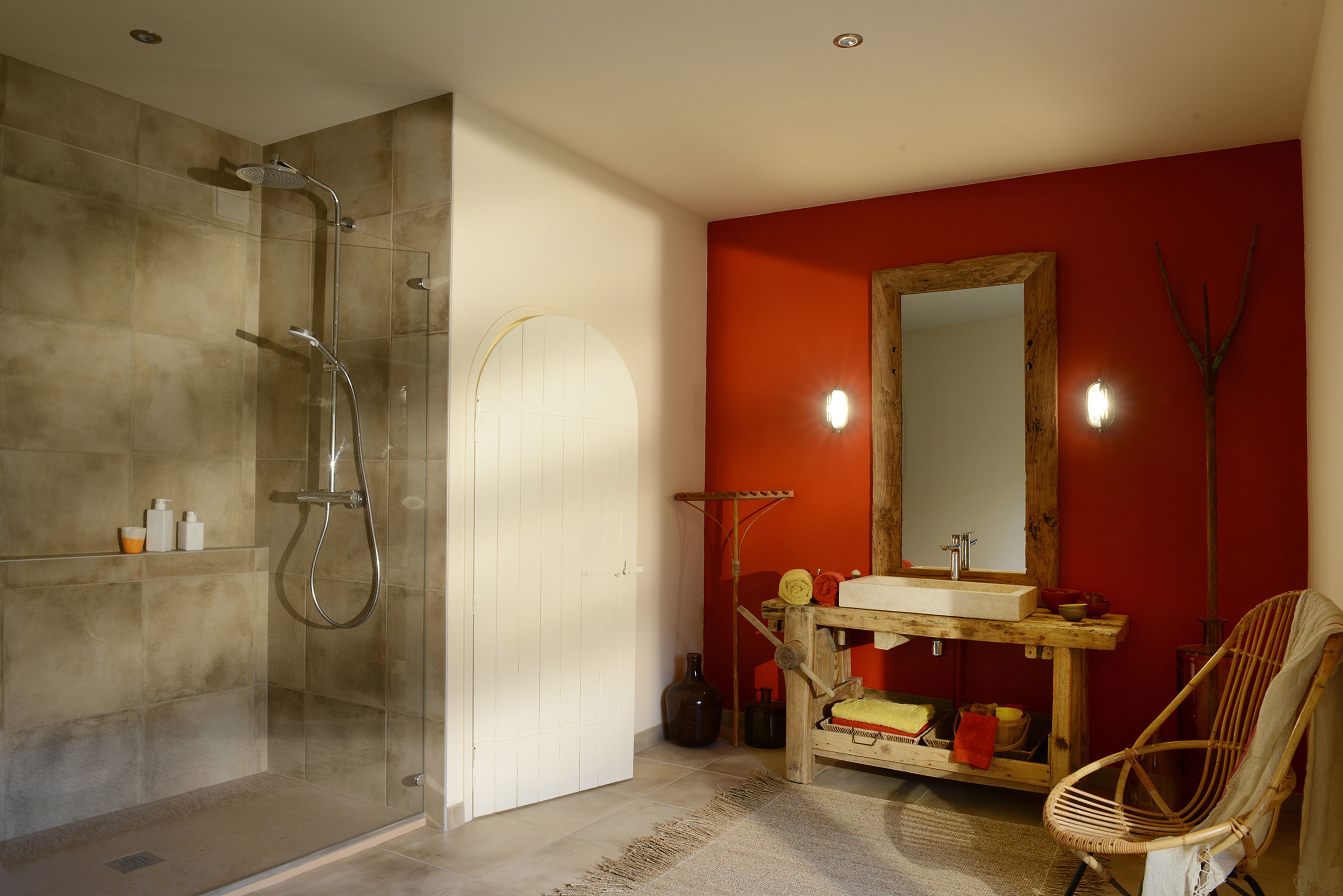 Un baño con ducha de vidrio, tocador de madera con espejo y una silla de mimbre.