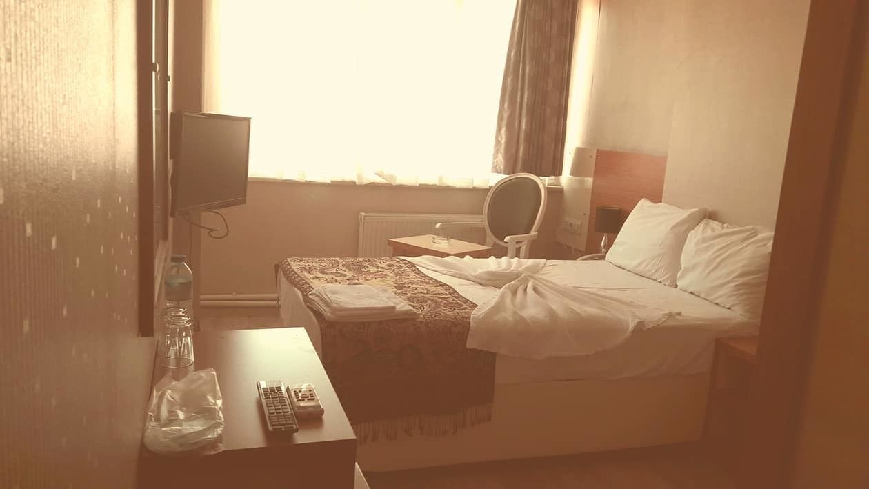 A hotel room with a bed, a desk with a remote control, a chair, a television, and a window with curtains.