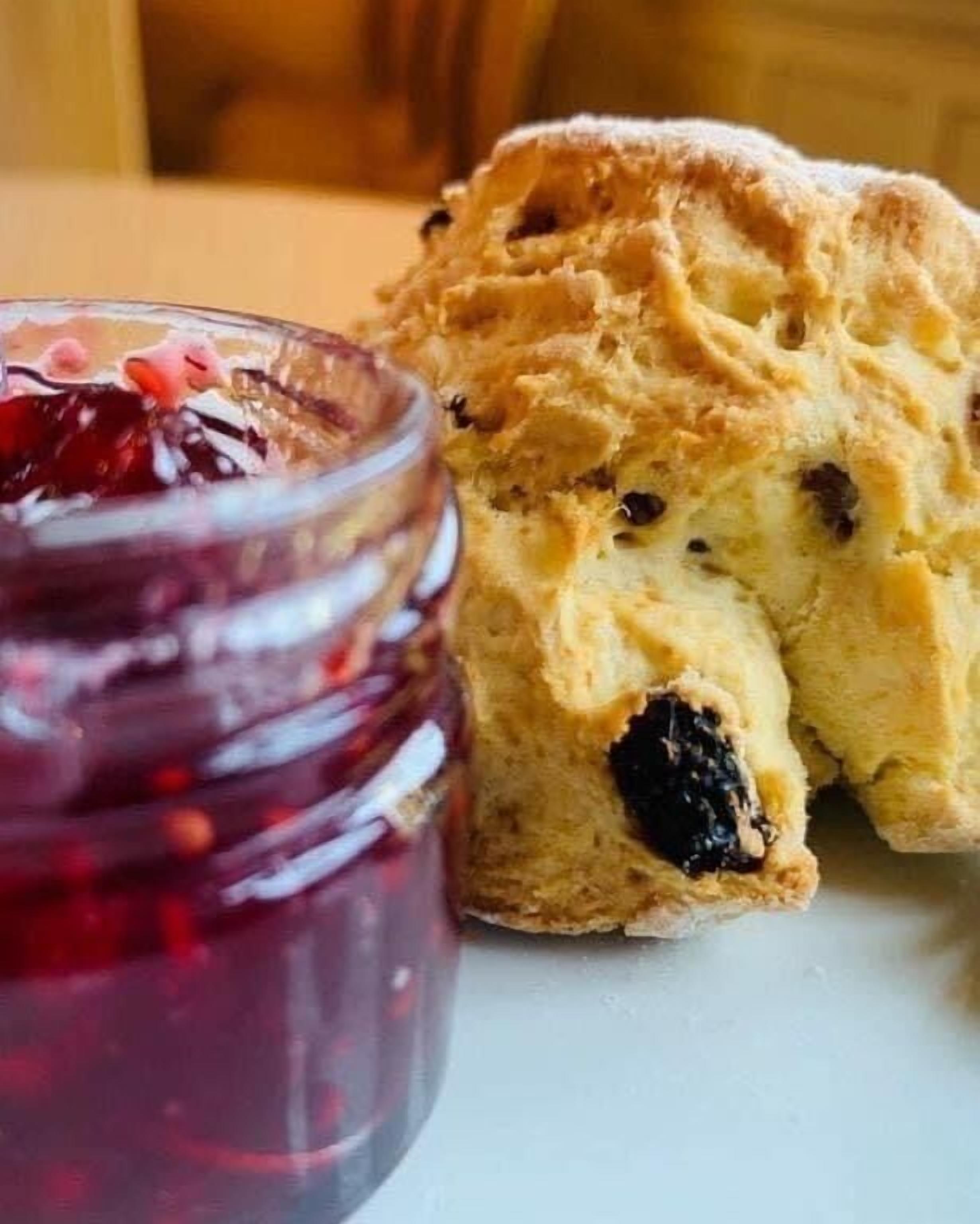 A close-up of a scone with a berry jam jar beside it.