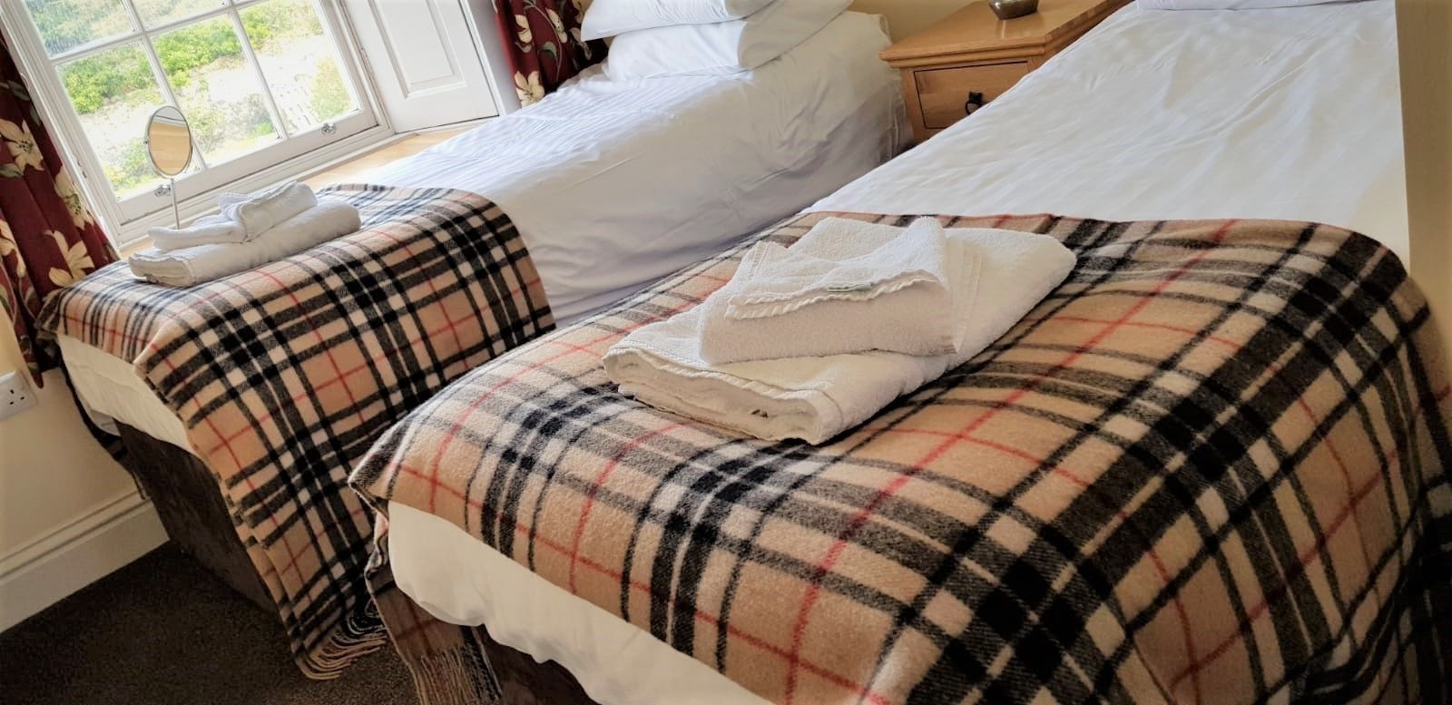 A hotel room with two beds, one with a plaid bedspread and the other with plain white linens.