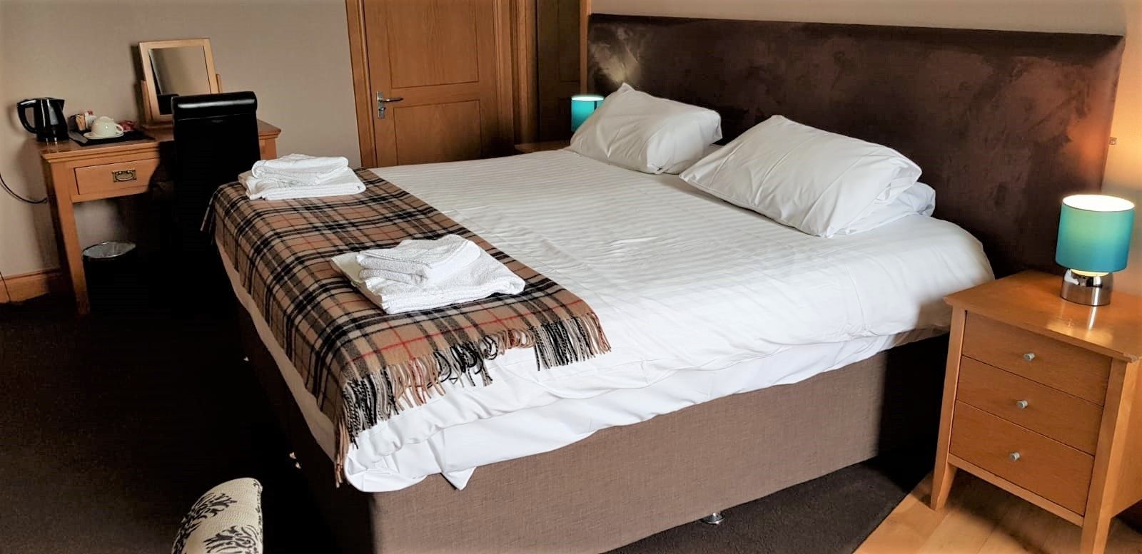 A neatly made bed with a plaid blanket, a bedside lamp, and a wooden nightstand with drawers.